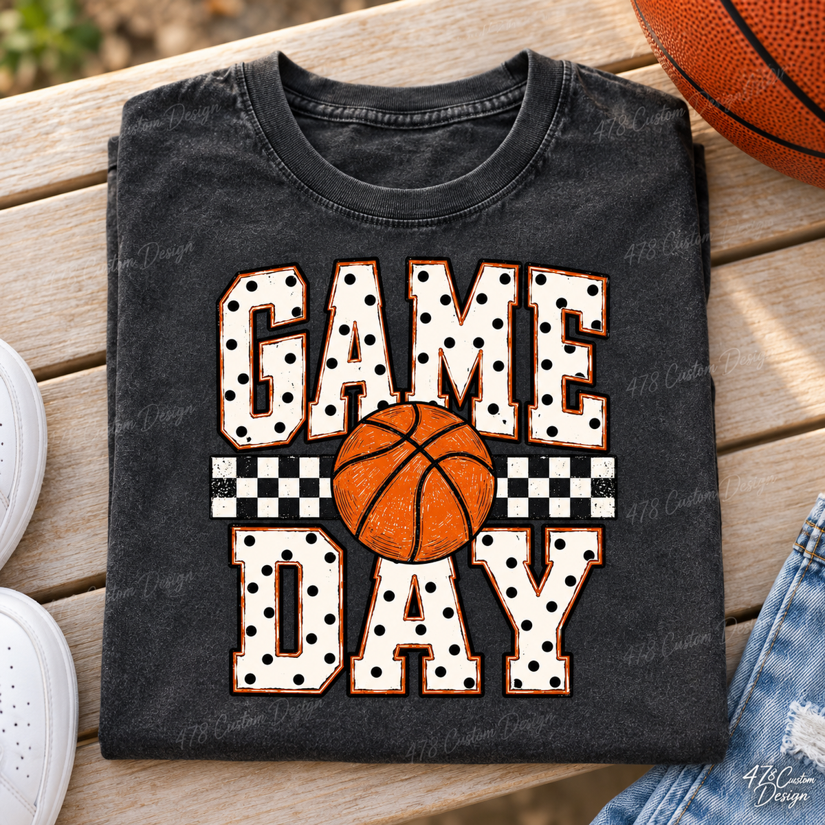 Cream varsity GAME DAY lettering with black polka dots, orange outlines and a basketball over a checkerboard stripe. Shown on a folded pepper tee.