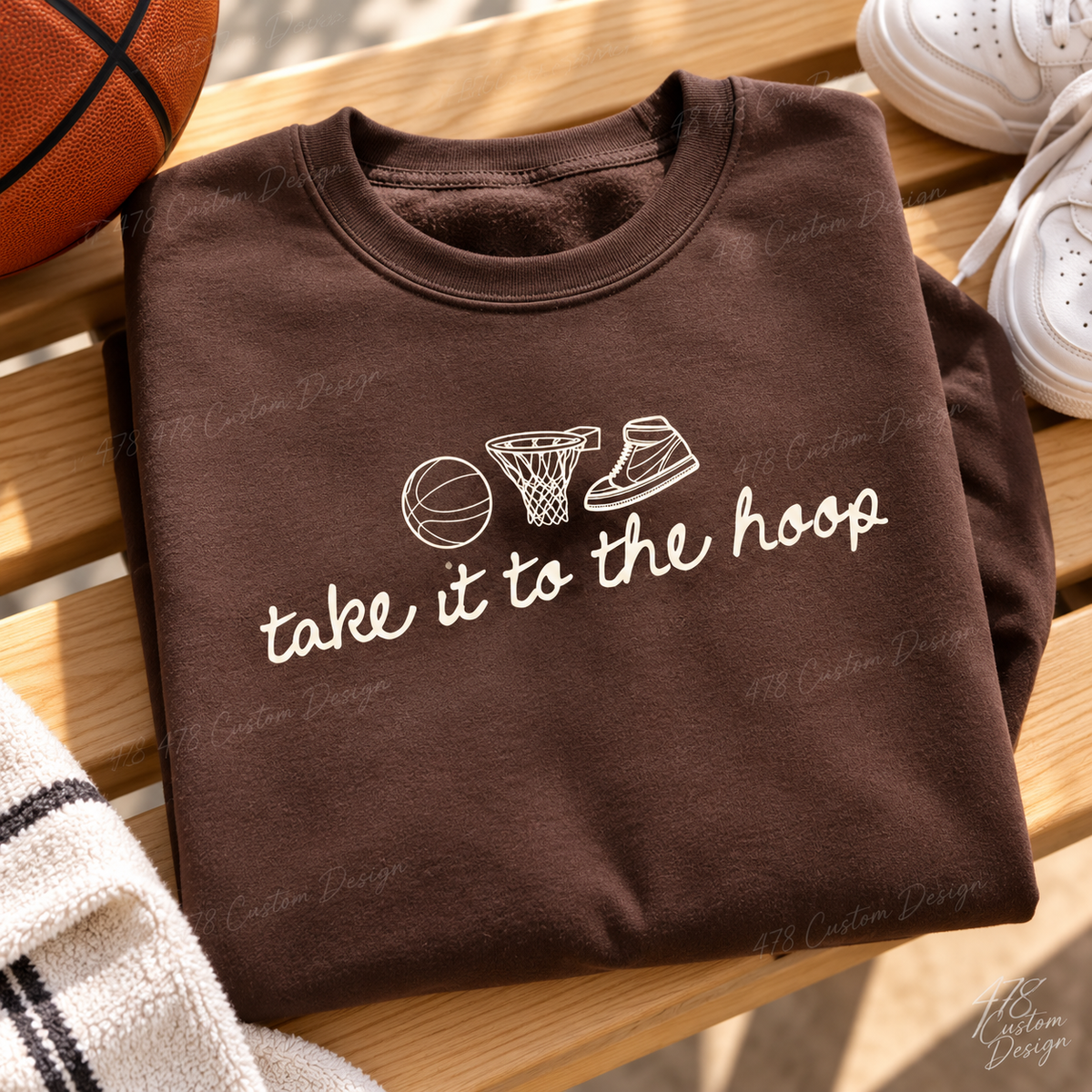 Cream basketball, hoop and high-top sneaker line art with handwritten take it to the hoop script. Shown on a chocolate brown crewneck sweatshirt.