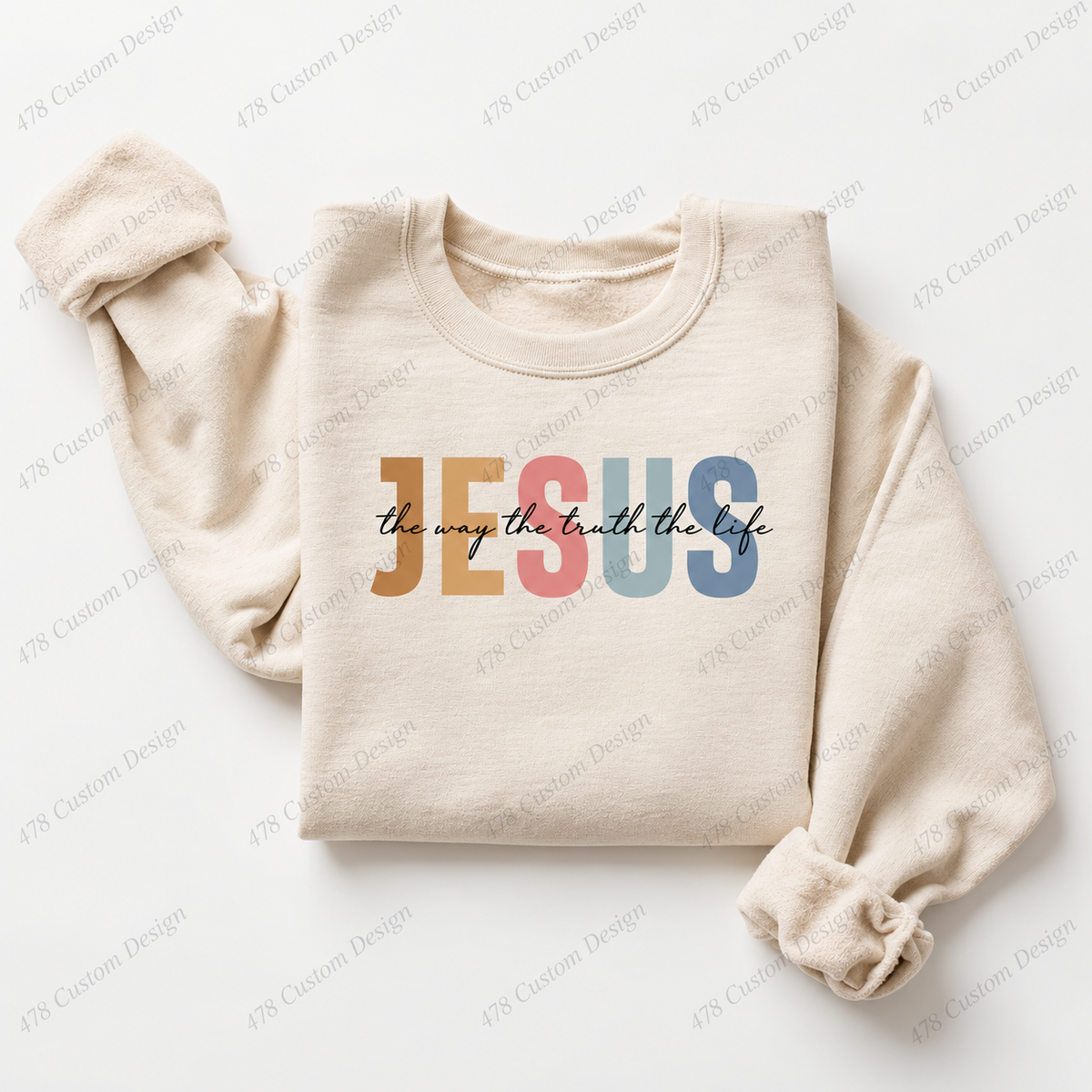 Folded cream sweatshirt with muted multicolor JESUS lettering and black the way the truth the life script