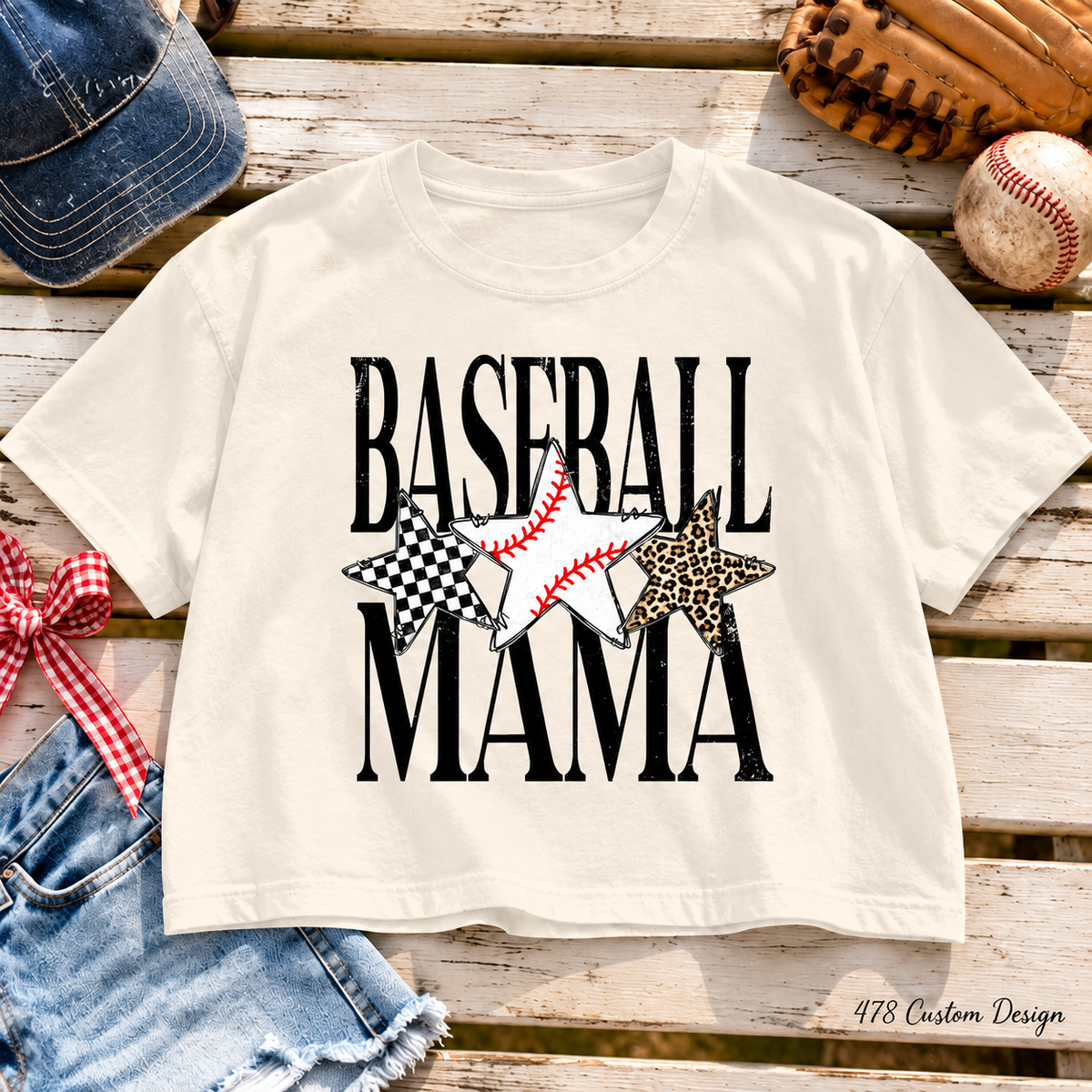 Black distressed Baseball Mama lettering with checkerboard, baseball and cheetah stars. Shown on an ivory Comfort Colors boxy crop tee.