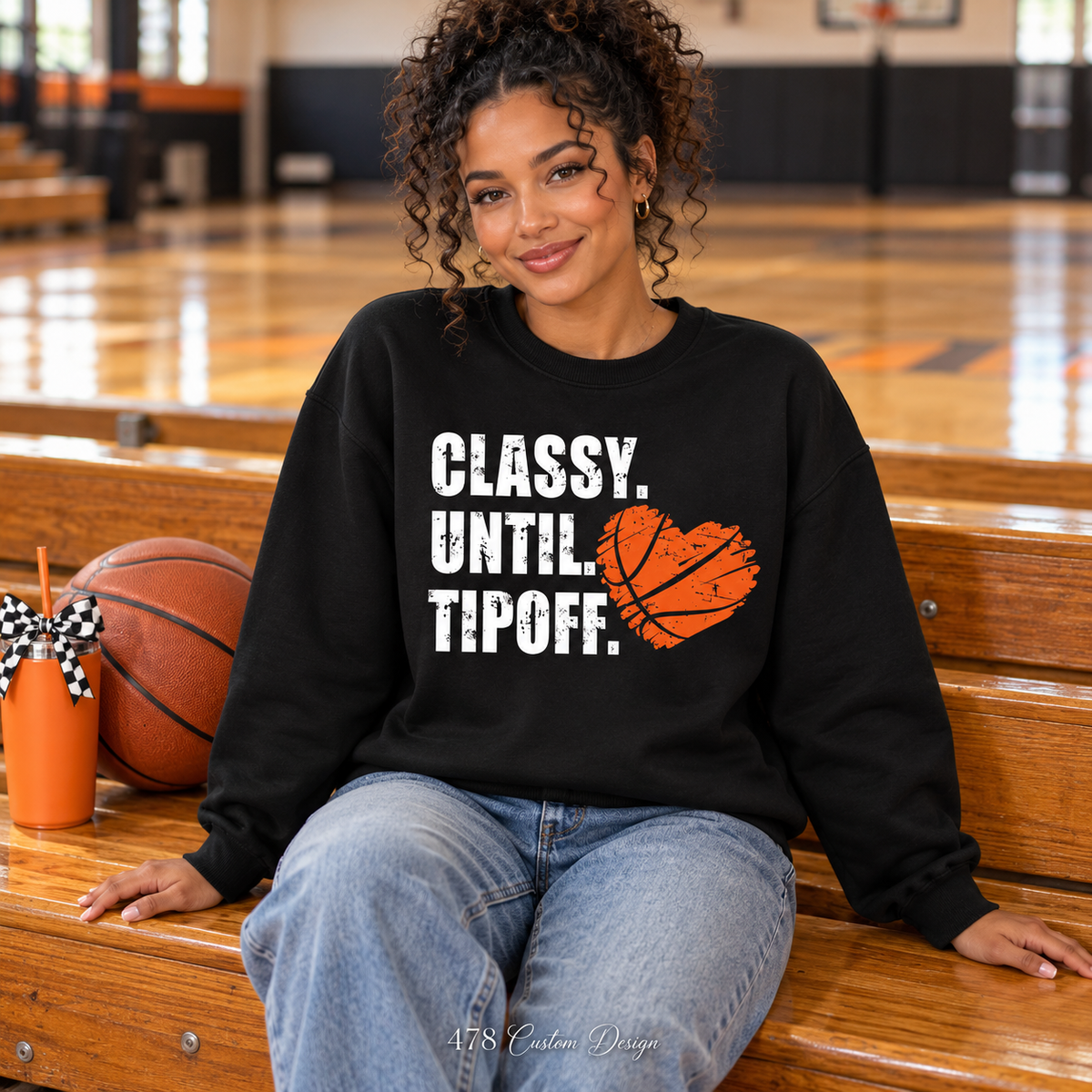 Woman seated courtside wearing black Classy Until Tipoff basketball heart sweatshirt