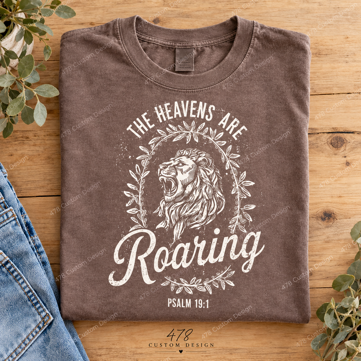Folded brown shirt with cream The Heavens Are Roaring lion and wreath front design, Psalm 19:1